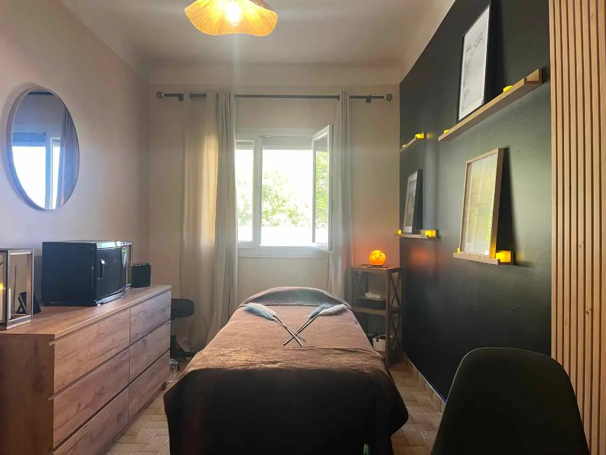 La salle de massage du Cabinet Phoenix à Cabestany : table de soin, lumière douce, murs sombres